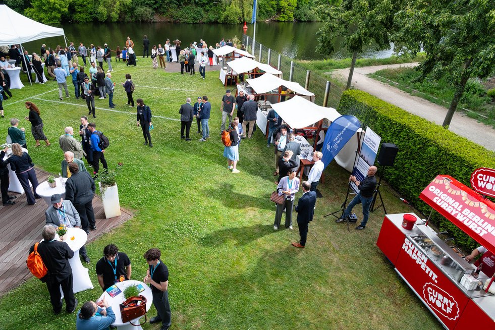 Luftaufnahme einer BPW-Netzwerkveranstaltung mit Catering- und Informationsständen am Wasser. Teilnehmende knüpfen Kontakte und tauschen sich in entspannter Atmosphäre aus.