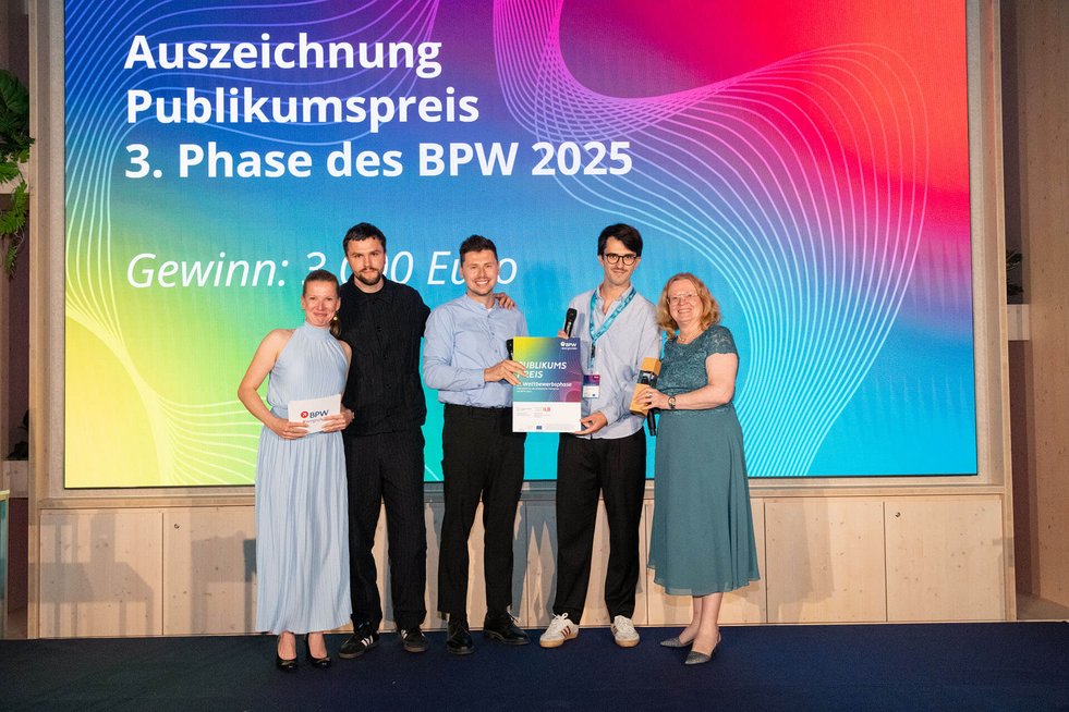 Gründertrio erhält einen Preis, daneben stehen die Moderatorin sowie die Laudatorin Friederike Haase aus dem Wirtschaftsministerium Brandenburg