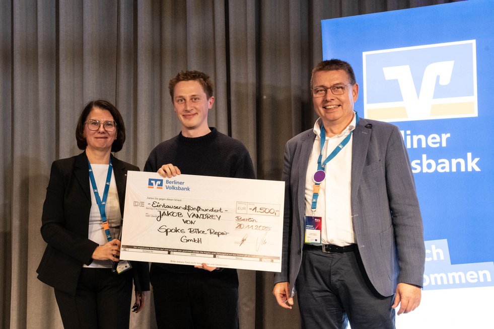 Drei Personen stehen auf einer Bühne und halten einen übergroßen Scheck in den Händen 