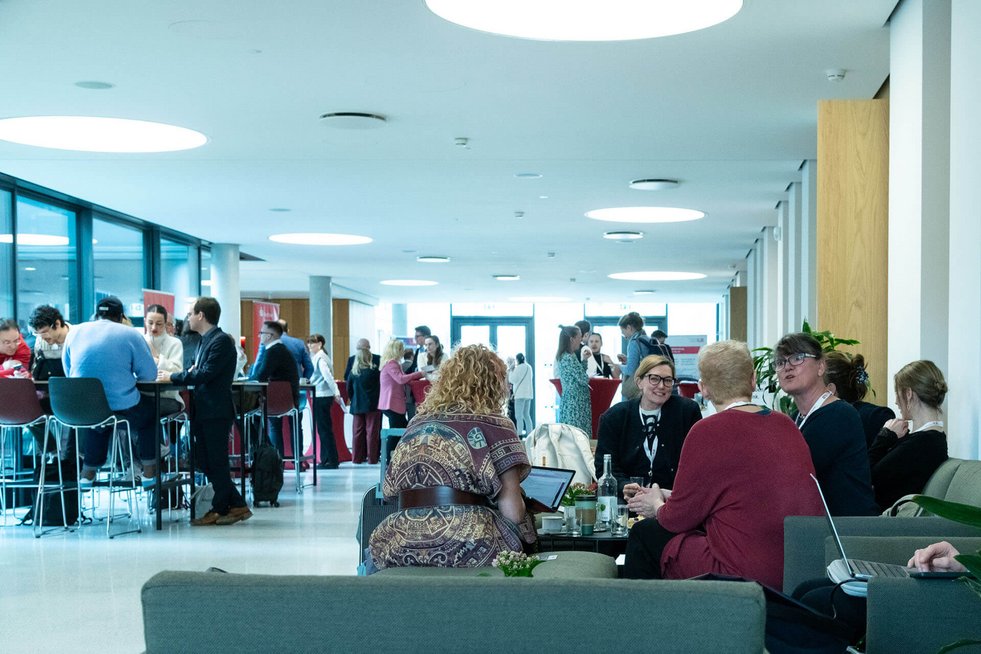 Menschen sitzen auf Möbeln in einem Foyer und sprechen miteinander