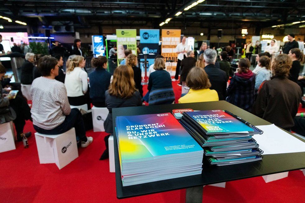 Blick auf den Marktplatz der Messe deGUT - Gäste sitzen auf Hockern und blicken zur Bühne