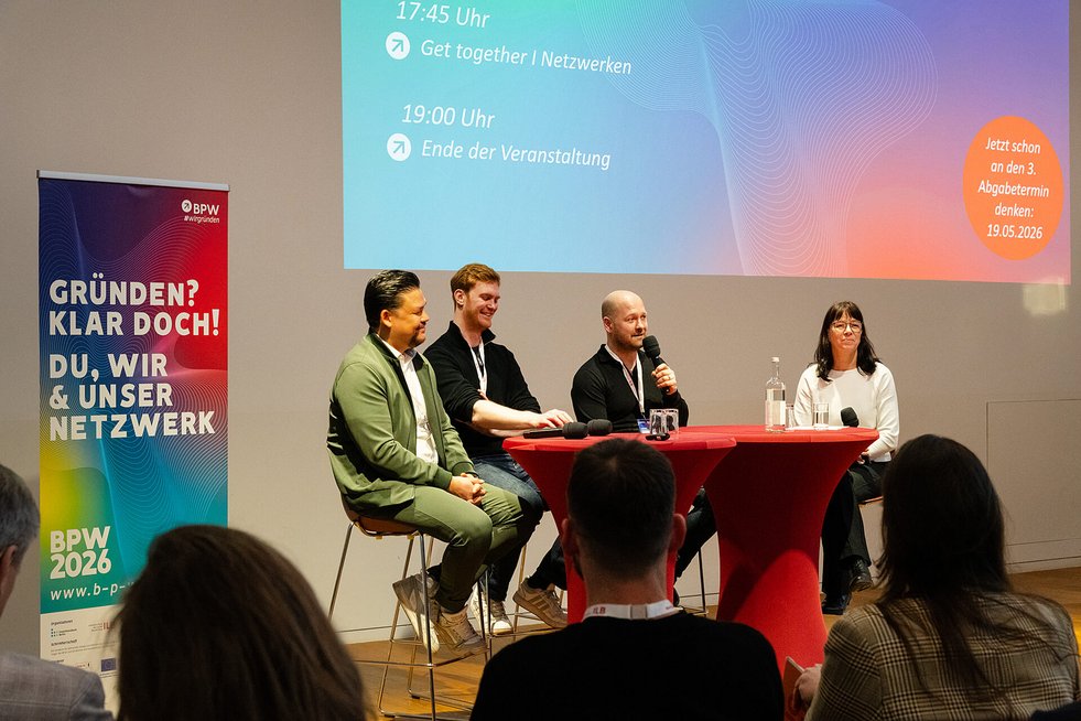 Vier Personen diskutieren auf einer Bühne vor Publikum.