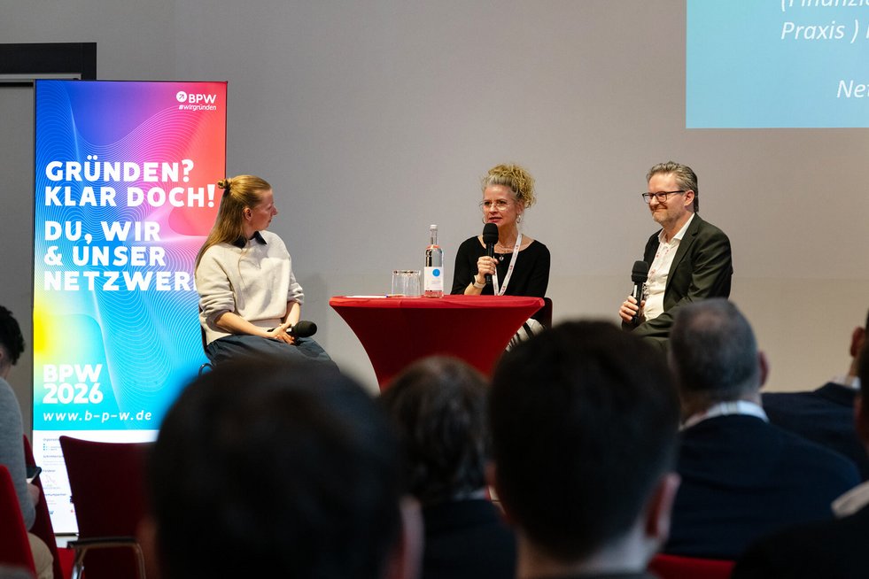 Podiumsdiskussion mit drei Personen auf einer Bühne.