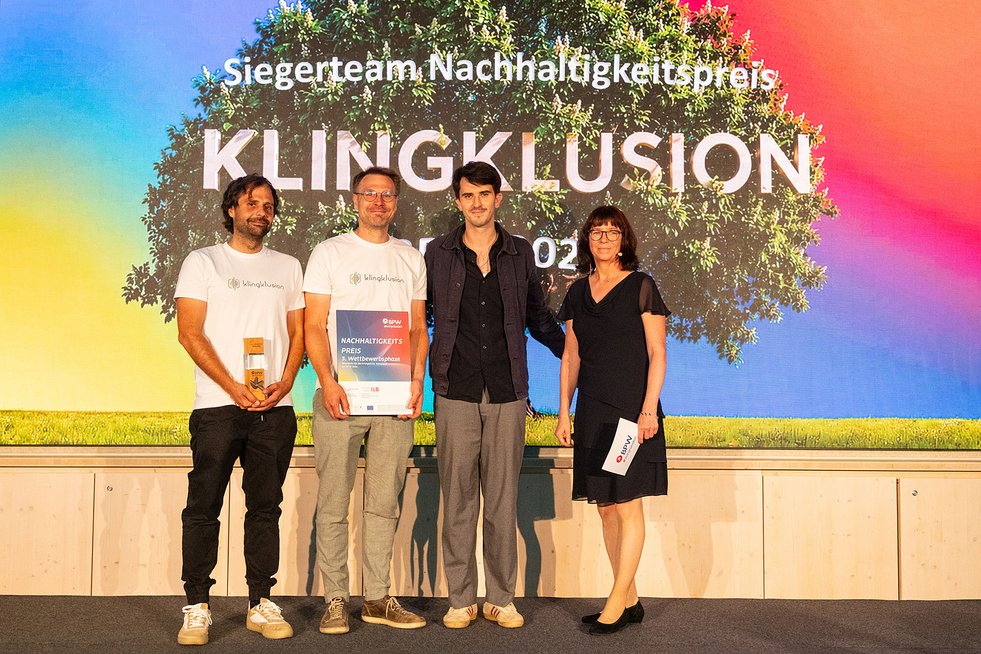 Vier Personen stehen auf einer Bühne bei der BPW-Prämierung. Das Siegerteam des Nachhaltigkeitspreises präsentiert Urkunde und Trophäe vor einer LED-Wand mit der Aufschrift „Siegerteam Nachhaltigkeitspreis – Klingklusion“.