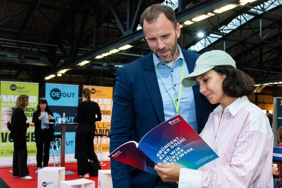 Zwei Personen stehen zusammen, eine Frau hält das BPW-Handbuch in den Händen und ein Mann blickt lächelnd in das Handbuch
