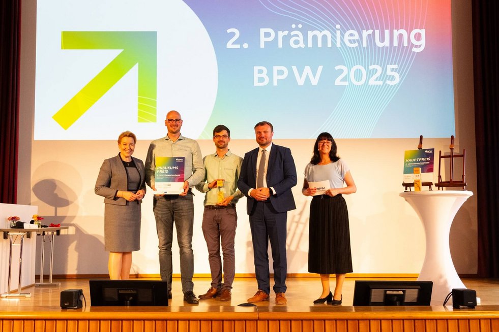 Fünf Personen stehen für ein Gruppenfoto zusammen, eine Person hält eine Urkunde, eine weitere Person hält einen Pokal