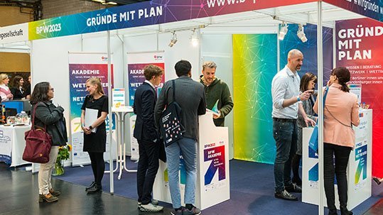 Gäste tummeln sich an einem Messestand und lassen sich beraten