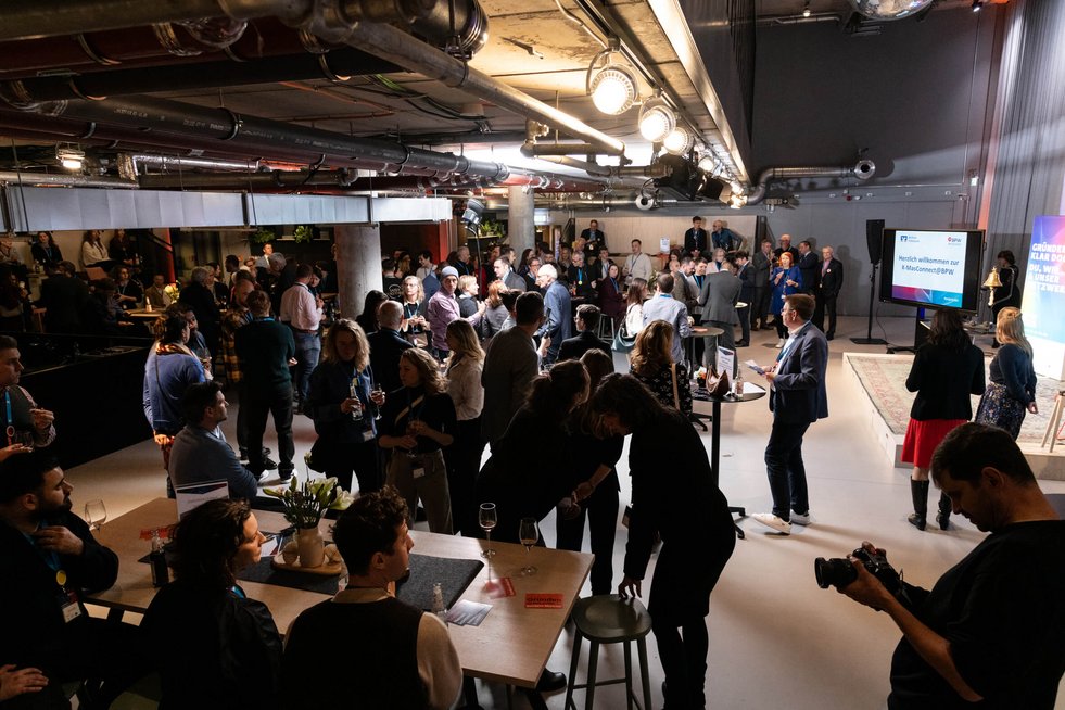 Blick in einen Veranstaltungssaal, viele Menschen stehen zusammen und tauschen sich aus