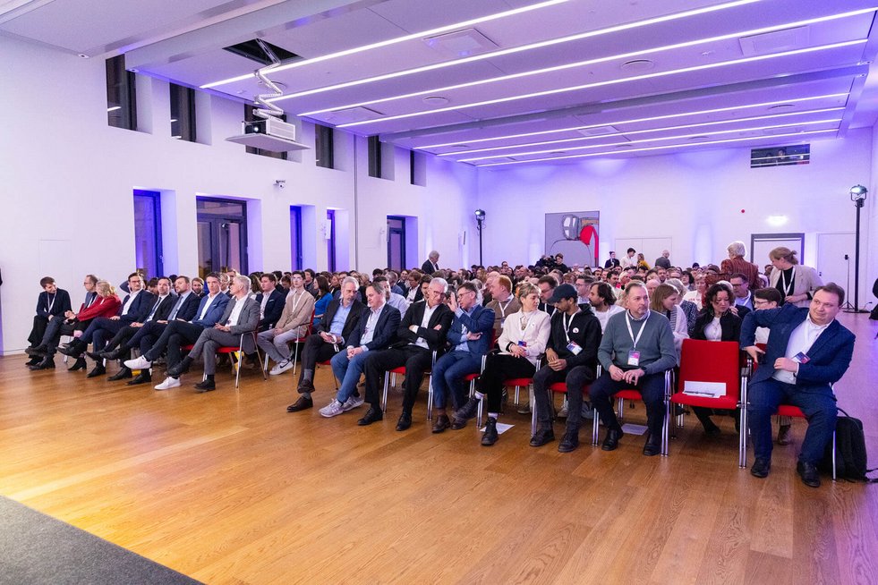 Großer Veranstaltungsraum mit vielen sitzenden Personen in Reihen. Das Publikum wartet auf den Beginn oder die Fortsetzung eines Programmpunkts.