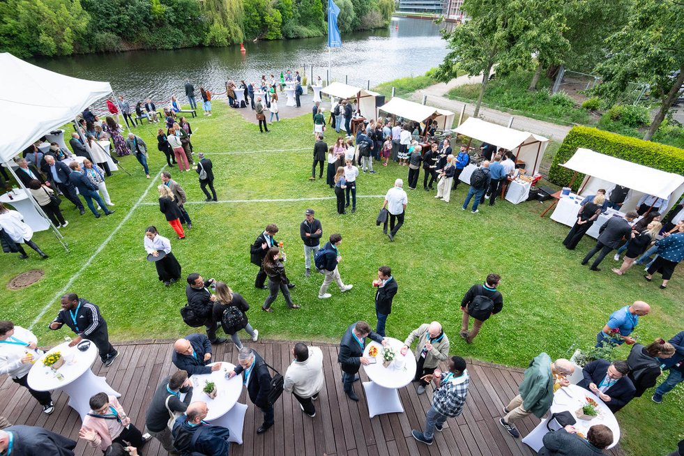 Luftaufnahme einer Netzwerkveranstaltung des Businessplan-Wettbewerb Berlin-Brandenburg (BPW) mit zahlreichen Teilnehmenden, Catering-Ständen und Austausch am Ufer.