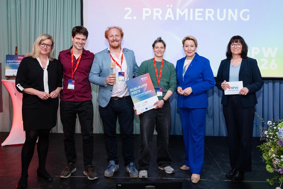 Sechs Personen auf einer Bühne mit Urkunde und Trophäe bei einer Preisverleihung.