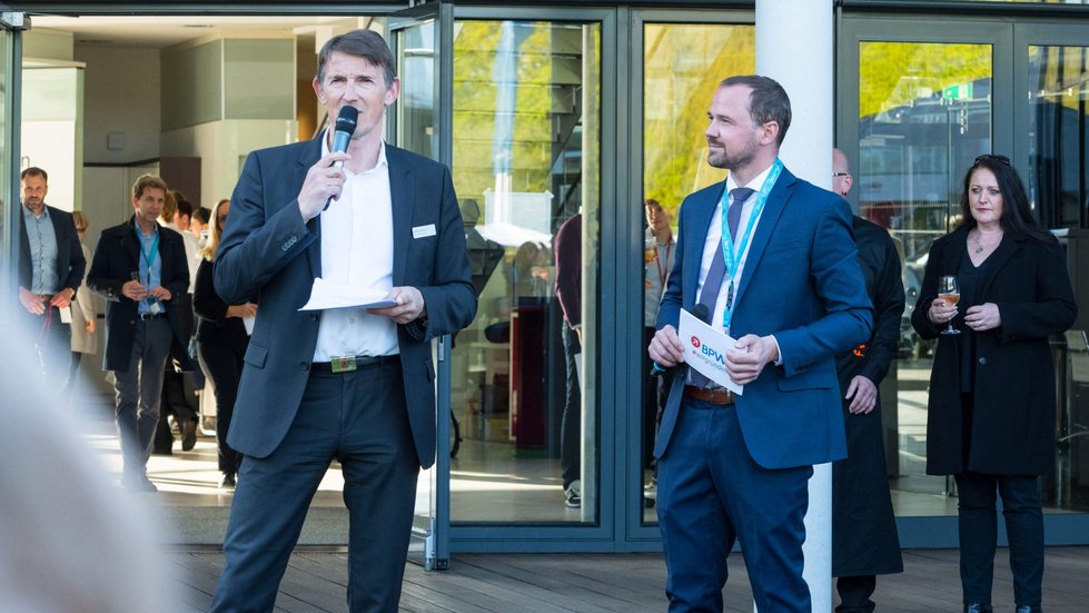 Gastgeber steht neben Moderator und spricht ins Mikrofon