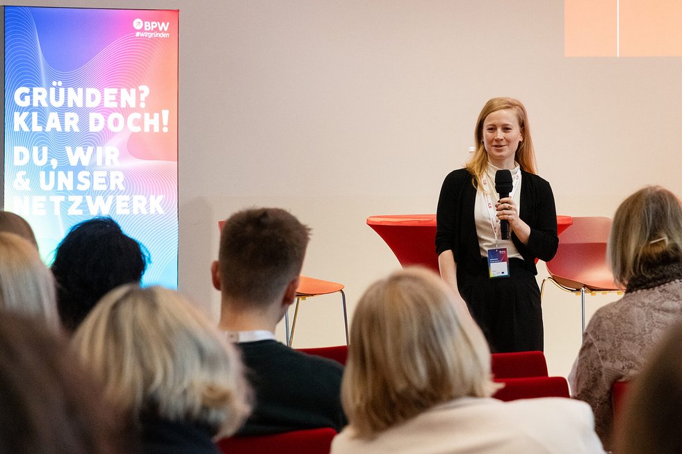 Frau mit Mikrofon präsentiert auf einer Bühne.