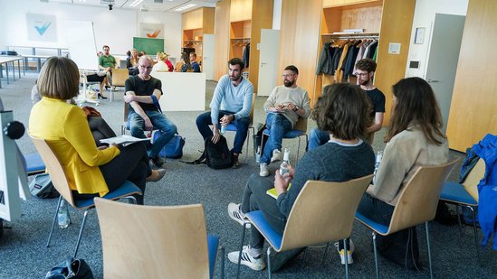 Teilnehmer:innen sitzen in einem Kreis und sprechen miteinander