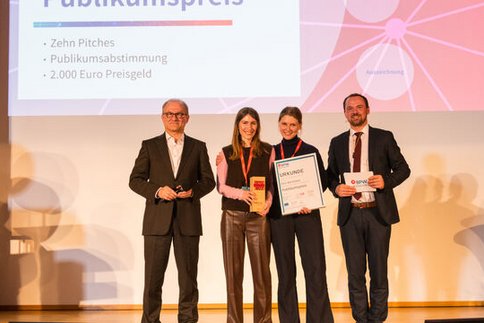 Zwei Gründerinnen umrahmt vom Moderator und dem Laudator bei der Überreichung einer Urkunde