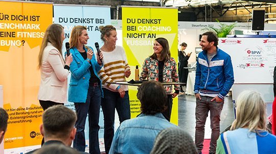 Talkrunde auf einer Bühne. Fünf Personen sprechen miteinander 