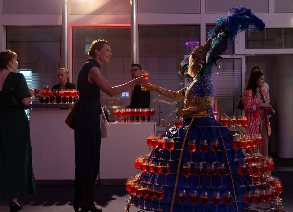 Eine Frau trägt ein Kleid voll mit Aperol-Gläsern als Showelement auf einer Preisverleihung