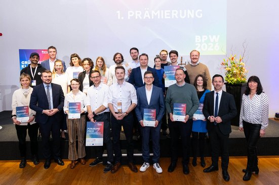 Große Gruppe von Personen auf einer Bühne bei einer Preisverleihung. Mehrere Teilnehmende halten Urkunden und Trophäen. Im Hintergrund ist die Aufschrift „1. Prämierung BPW 2026“ zu sehen.