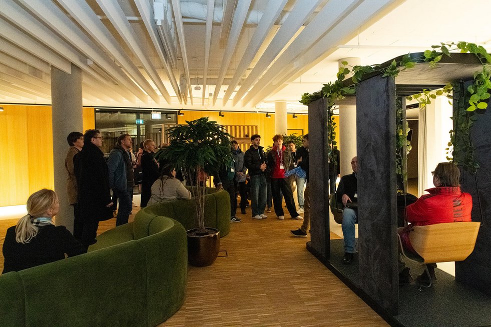 Gruppe von Menschen steht in einem modernen Innenraum mit Pflanzen und Sitzgelegenheiten.