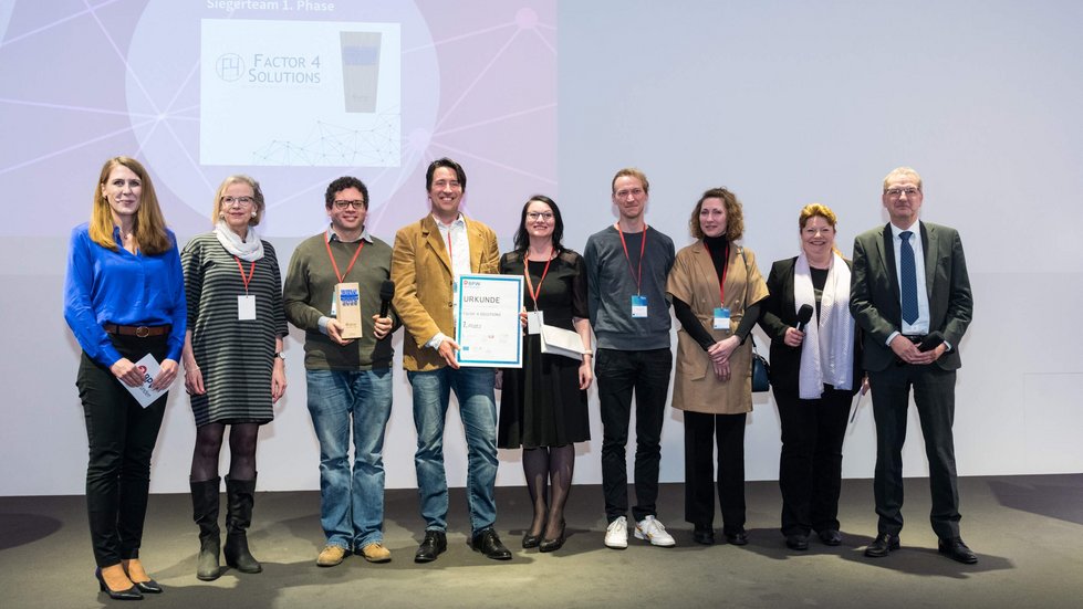 Das Siegerteam der ersten Phase steht für ein Gruppenfoto auf der Bühne, umrahmt von den Laudatoren und der Moderatorin