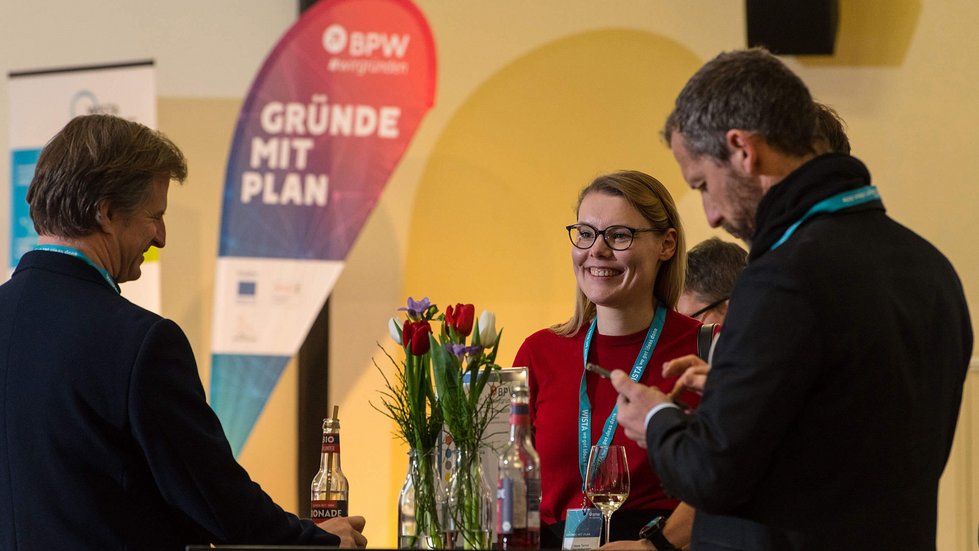 Drei Personen sprechen angeregt an einem Stehtisch miteinander.
