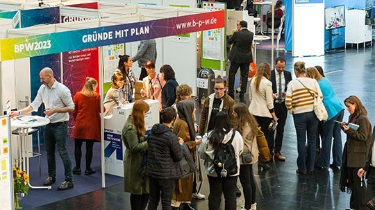 Viele Gäste stehen um einen Messestand herum und unterhalten sich
