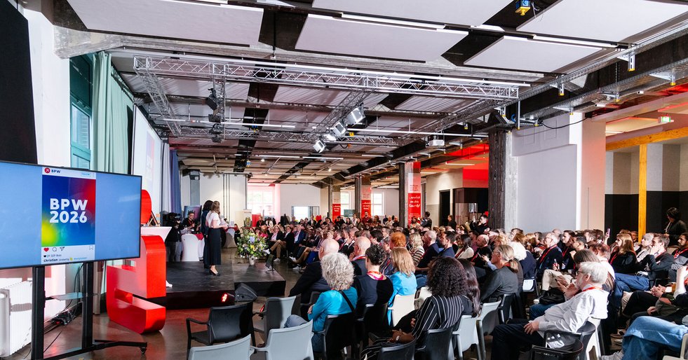 Große Veranstaltung mit Publikum vor einer Bühne und Präsentationsscreen „BPW 2026“.