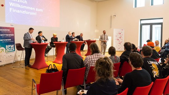 Finanzforum-2023-4 Podium mit vielen Expert:innen auf der Bühne, die ins Publikum sprechen