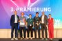 Verleihung Hauptpreis an das Team von Spree Monitoring, verliehen von Thomas Krause, Leiter der Abteilung Energie, Digitalisierung und Innovation in der Senatsverwaltung für Wirtschaft, Energie und Betriebe Berlin und Martina Klement Gewinnerteam und Gratulierende bei der dritten BPW-Prämierung auf der Bühne mit Urkunde und Trophäe.