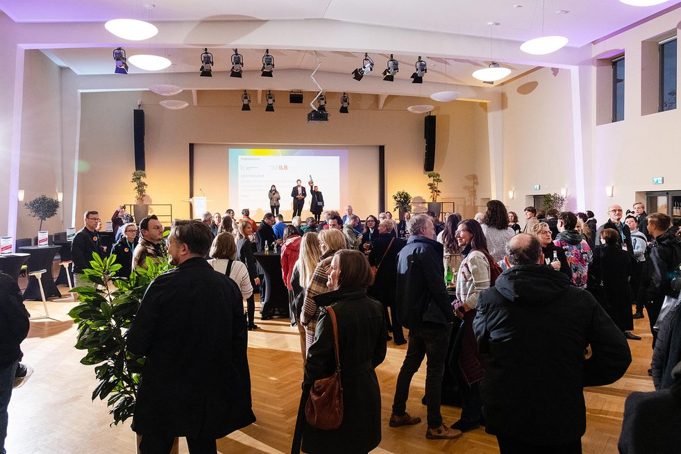 Zahlreiche Gäste stehen an runden Stehtischen und führen Gespräche, einige halten Getränke in der Hand.